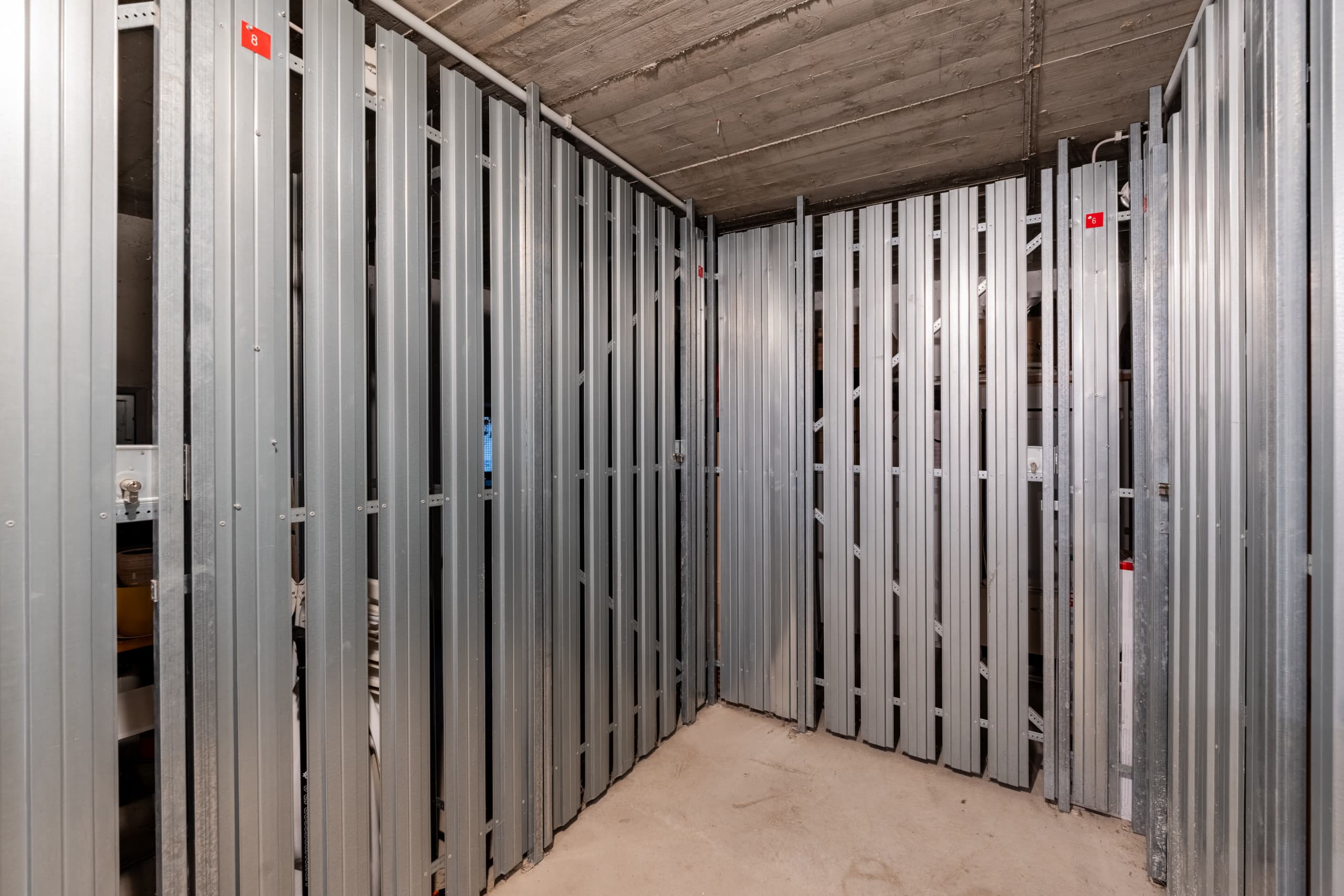 Blick in ein leerstehendes Kellerabteil mit grauen Metalltrennwänden und Betonboden
