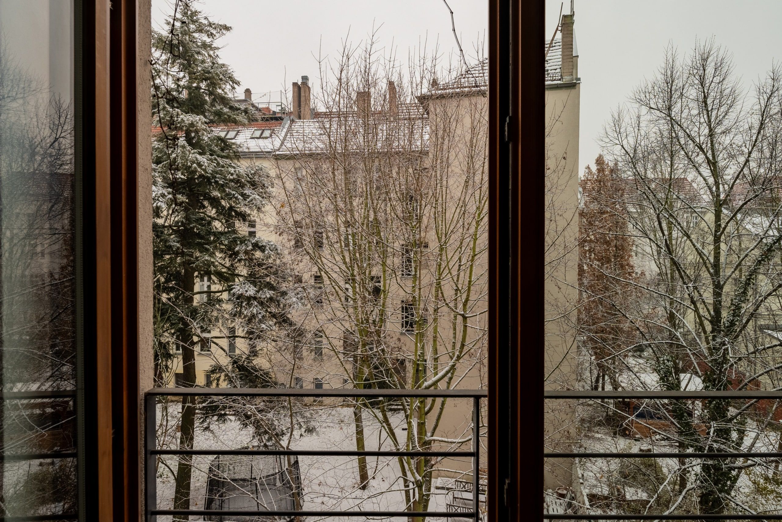 Ausblick vom Wohnungsbalkon auf verschneiten Innenhof mit Laubbäumen und mehrgeschossigen Wohnhäusern