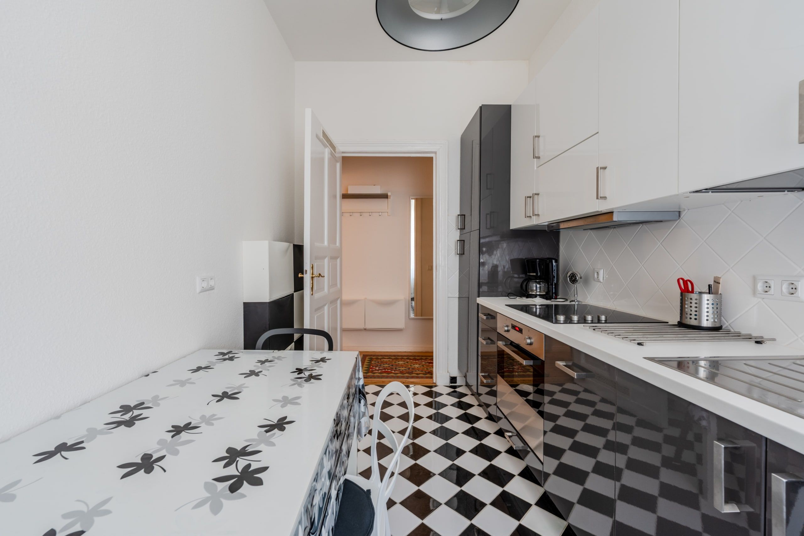 Innenansicht moderner Wohnungsküche mit Schachbrettboden, Einbauzeile, Esstisch mit Blumenmuster, Blick in den Flur