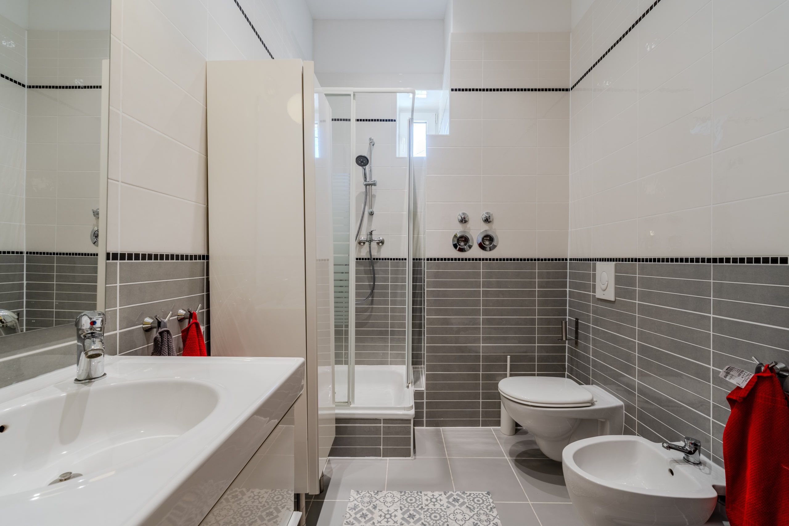 Innenansicht modernes Badezimmer mit grauen Wandfliesen und weißer Duschkabine aus Seitenperspektive