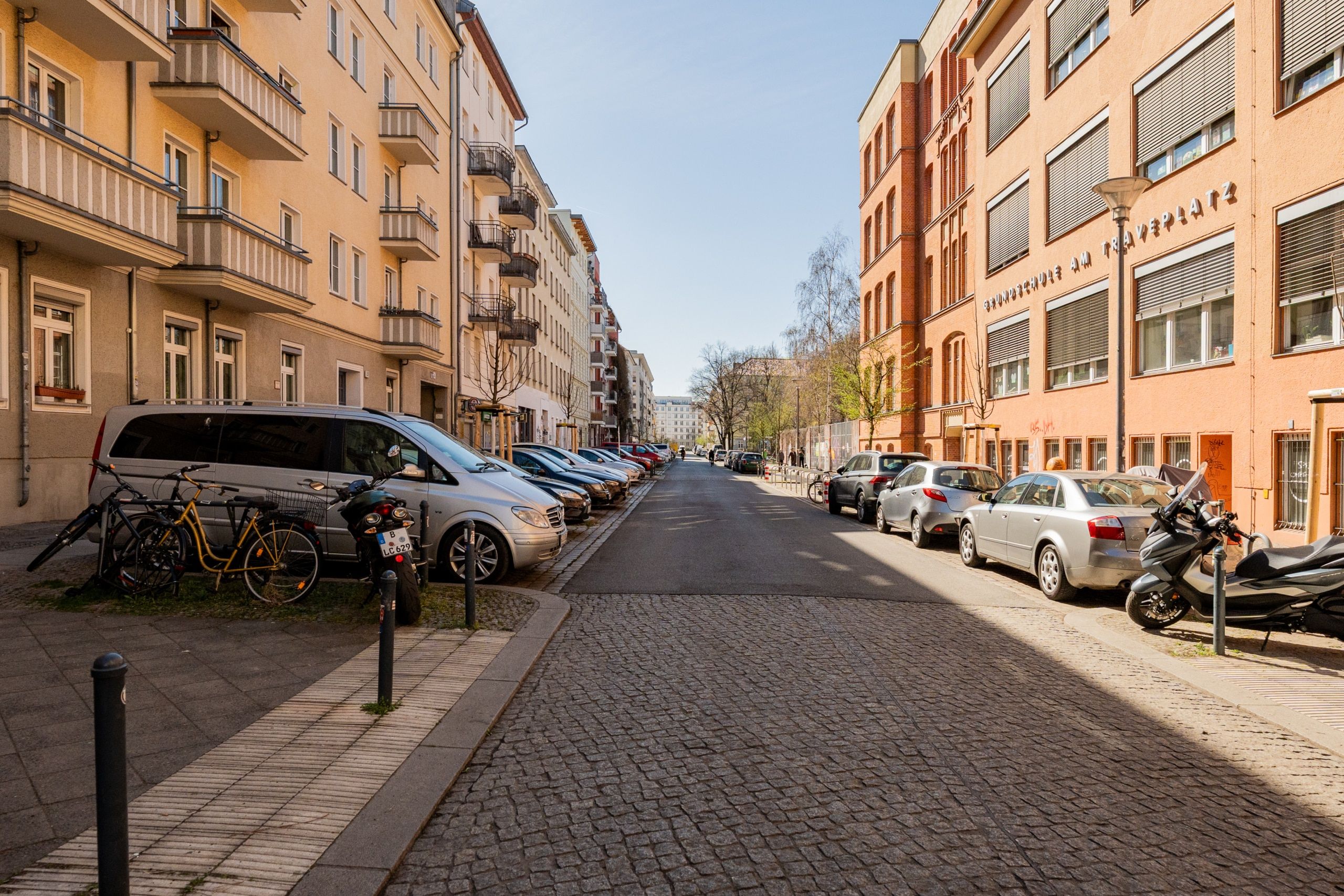 Straßenperspektive mit mehrgeschossigen Wohnhäusern mit Balkonen und Klinkerfassade neben geparkten Autos und Fahrrädern