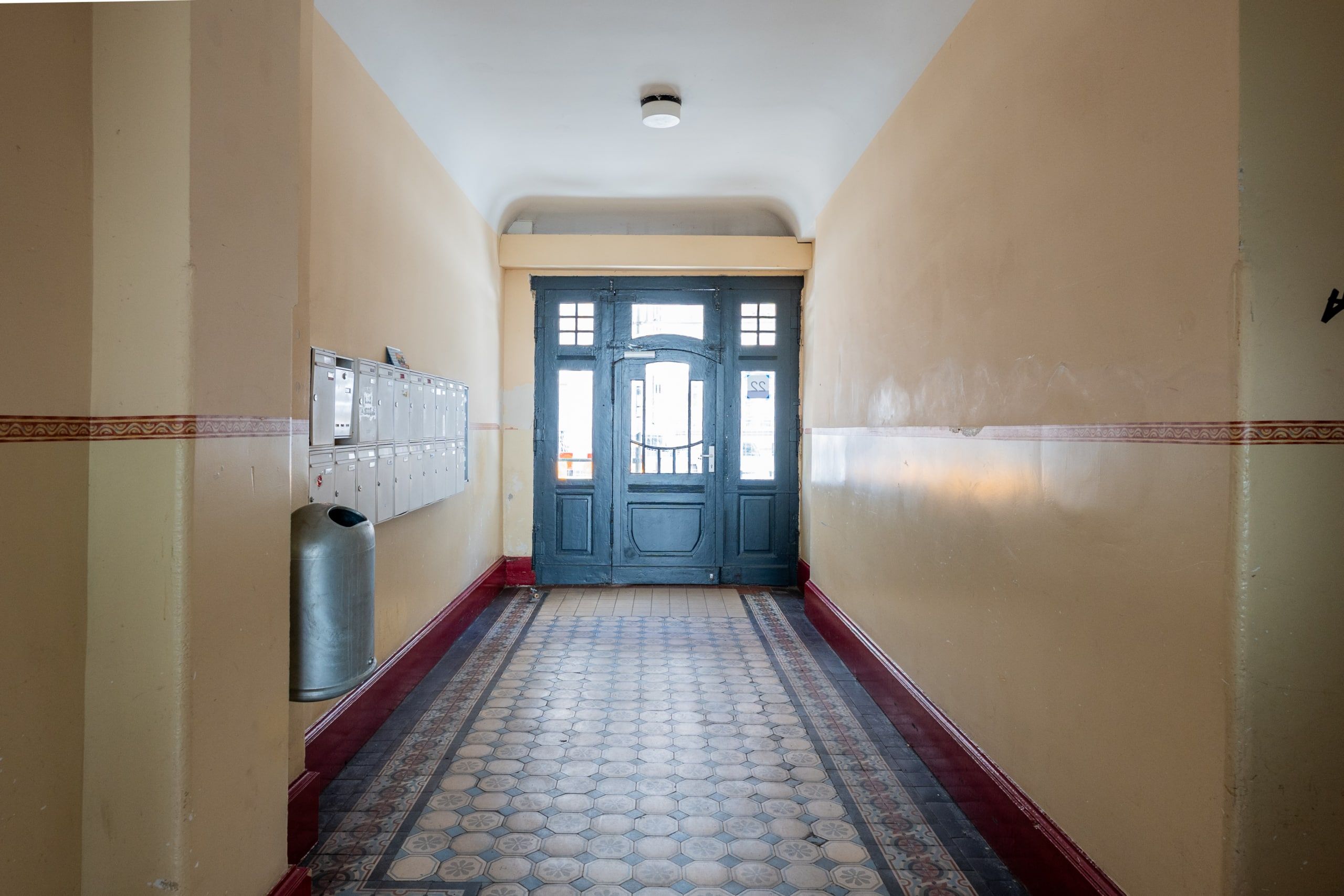 Eingangsfoyer eines Altbau-Mehrfamilienhauses mit bunten Mosaikfliesen an Boden Briefkästen und grüner Holztür