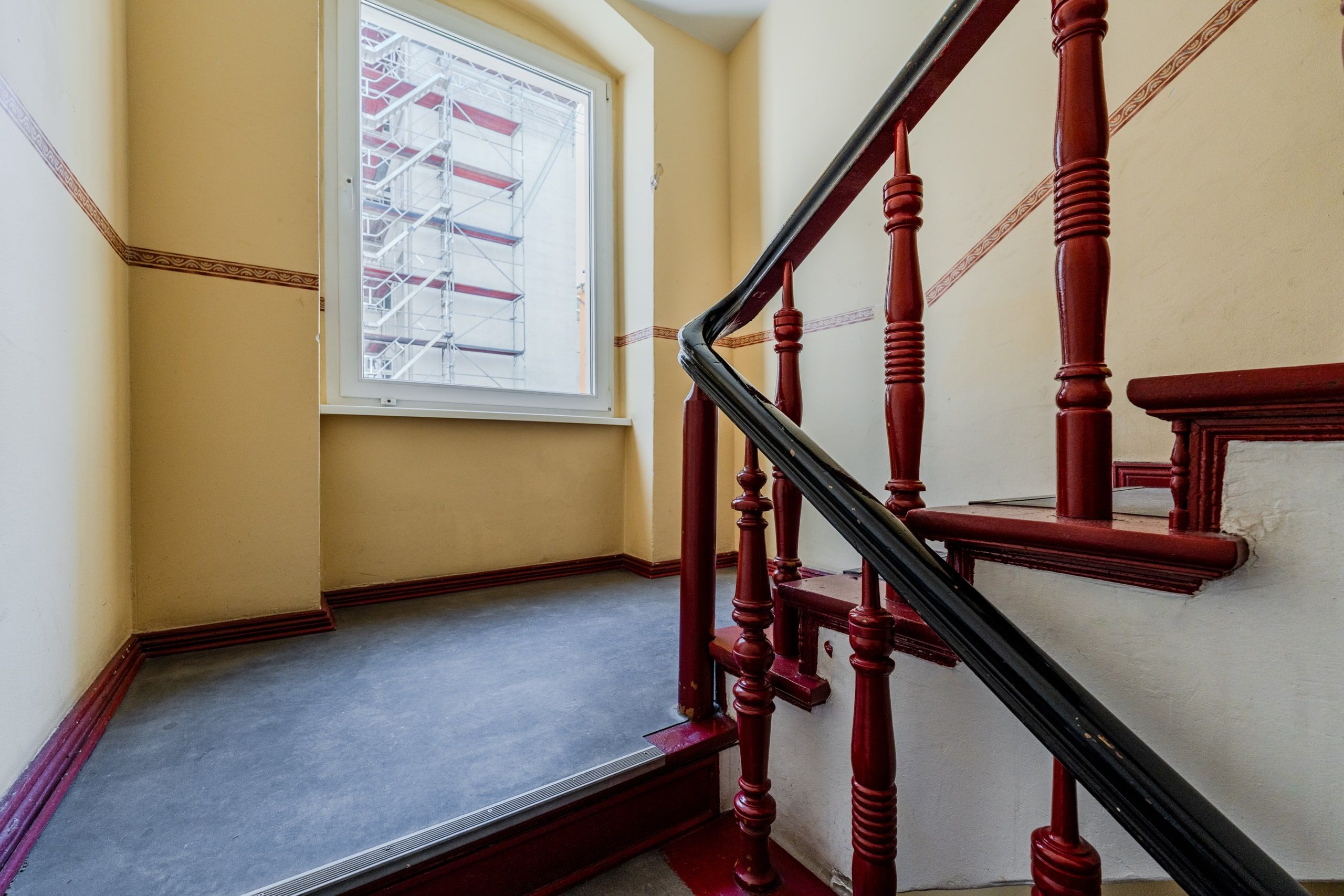Innenansicht Treppenhaus mit rotem Holzgeländer und Fenster mit Blick auf Gerüst
