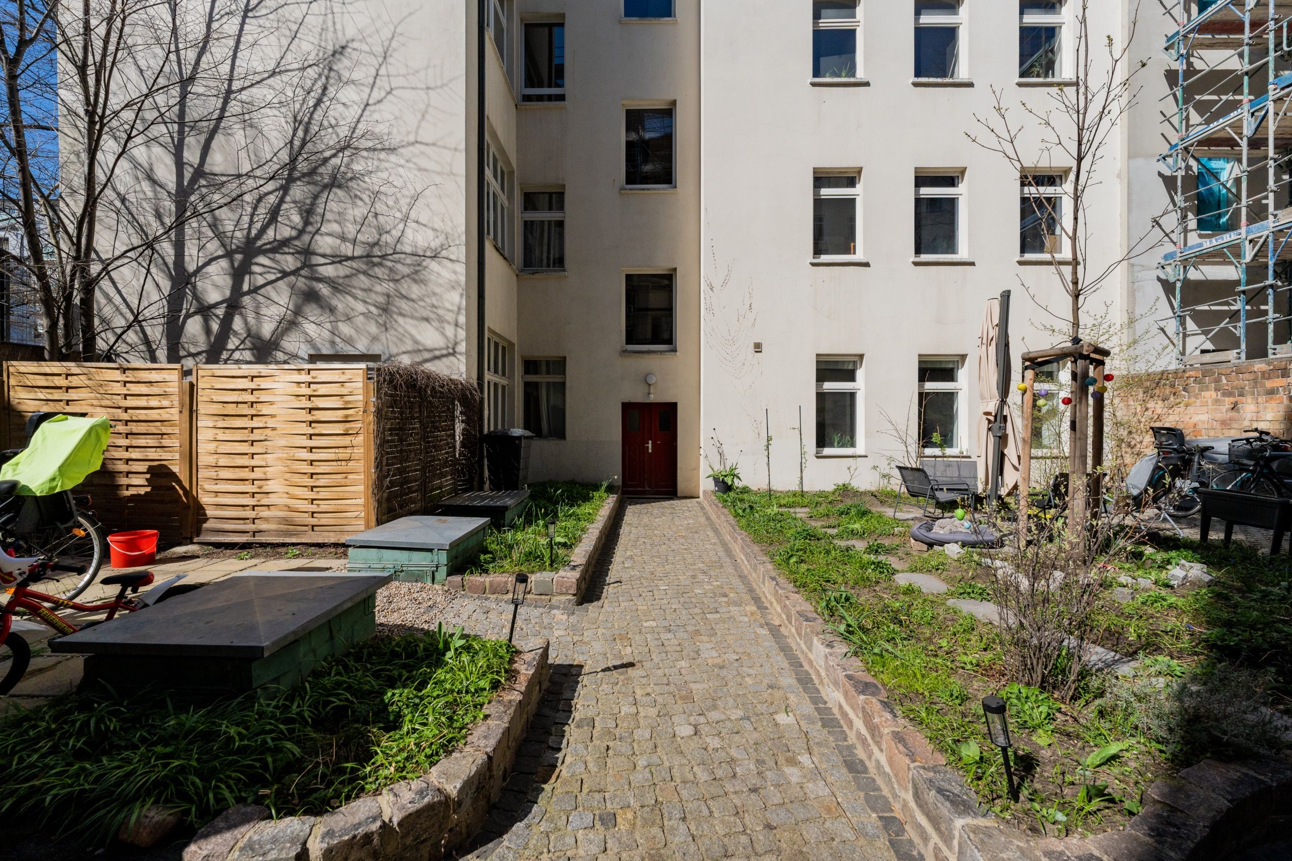 Innenhof eines Mehrfamilienhauses mit gepflastertem Weg, begrüntem Garten, Sitzbank und Hauseingang