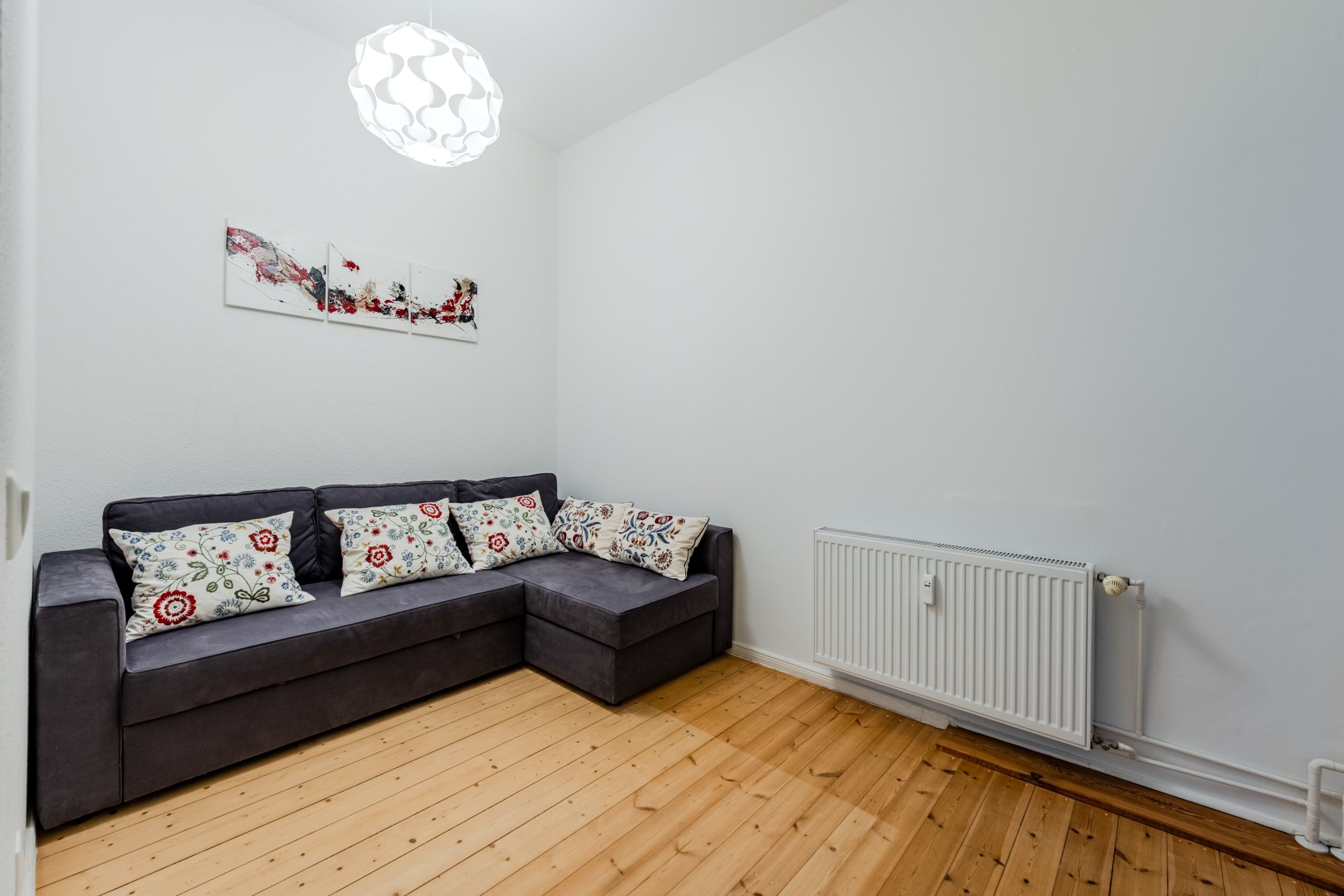 Blick ins Wohnzimmer mit L-Sofa, Holzdielen, Wandheizung, Pendelleuchte und abstraktem Wandbild