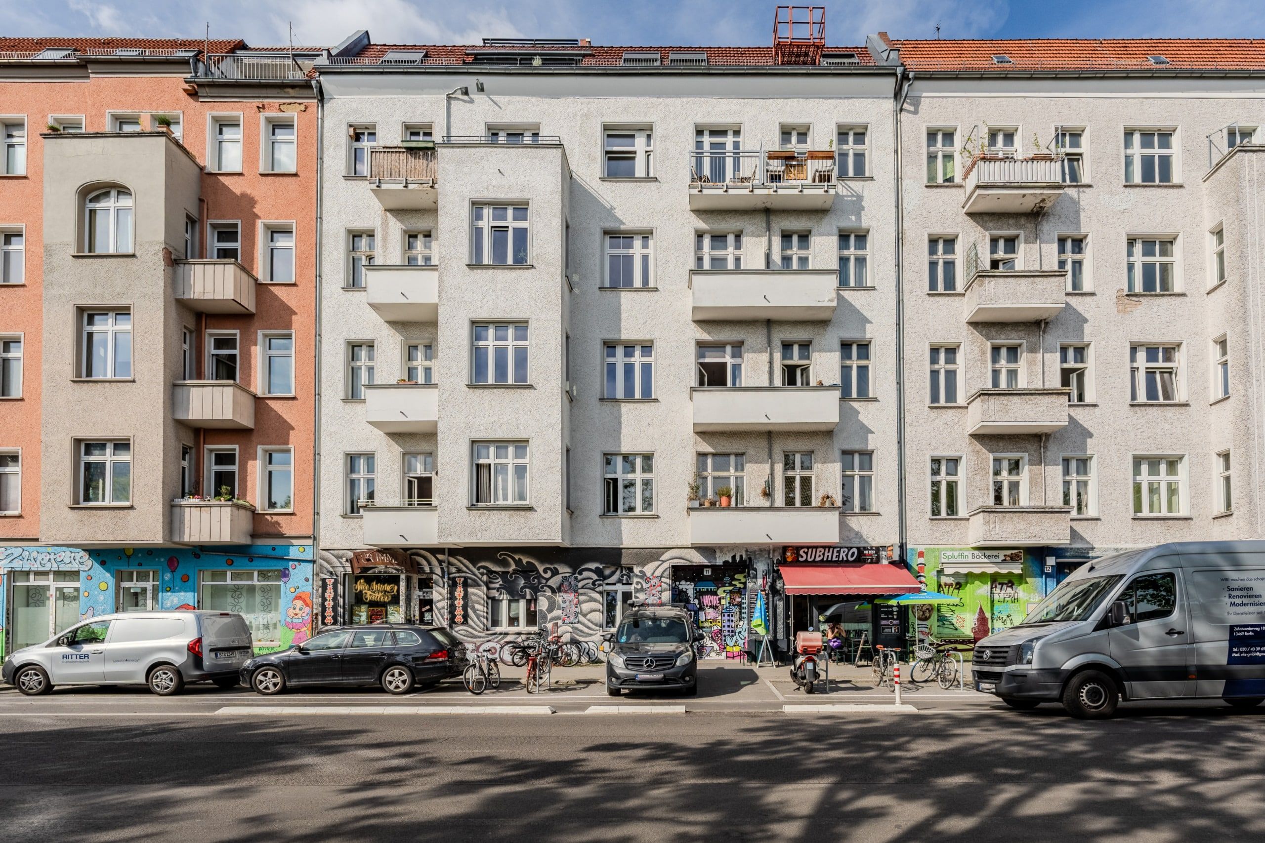 Frontalansicht mehrgeschossiges Wohnhaus mit Balkonen und bunten Graffiti-Läden im Erdgeschoss