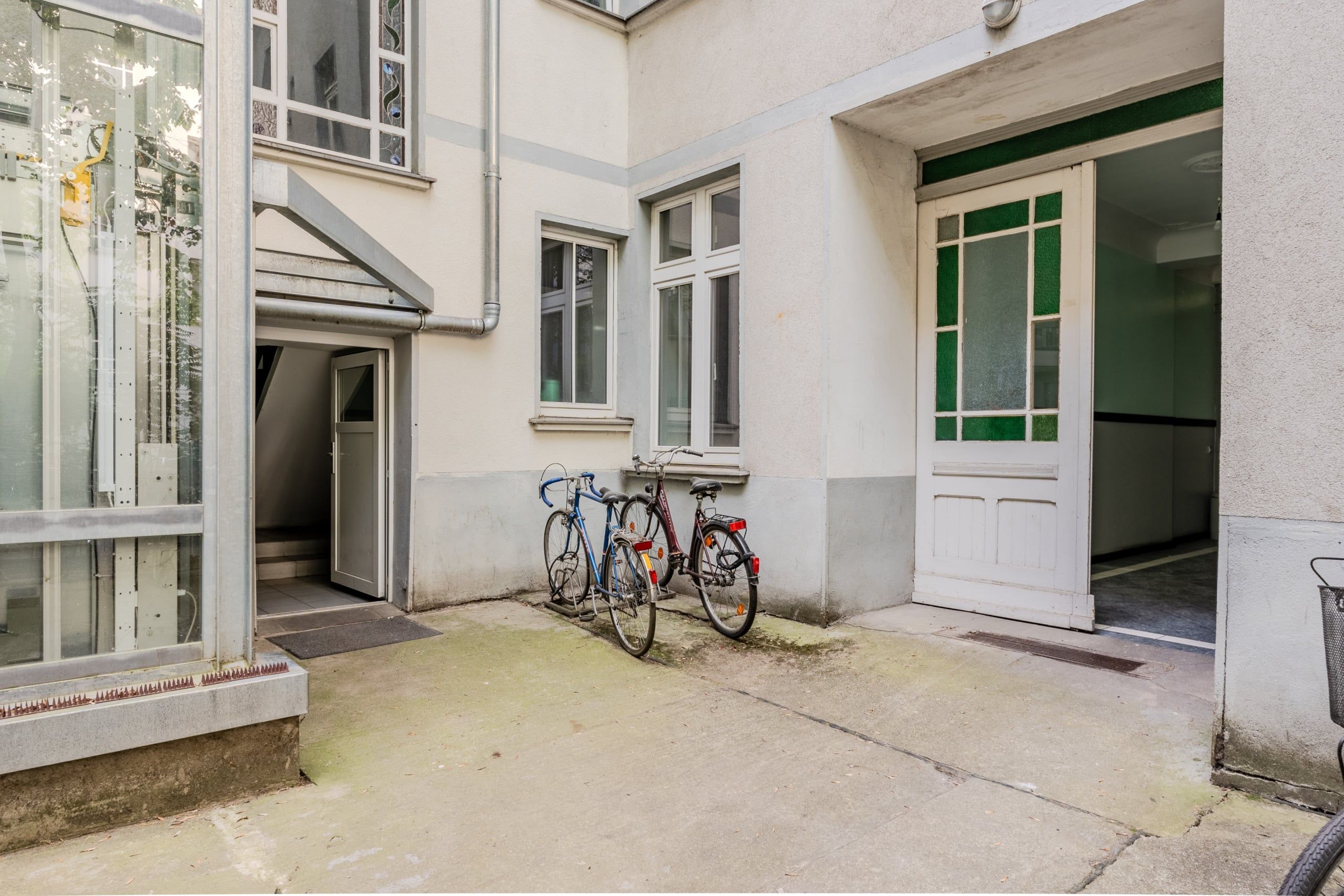 Innenhof eines Mehrfamilienhauses mit gläsernem Aufzug grünverglaster Eingangstür und zwei abgestellten Fahrrädern