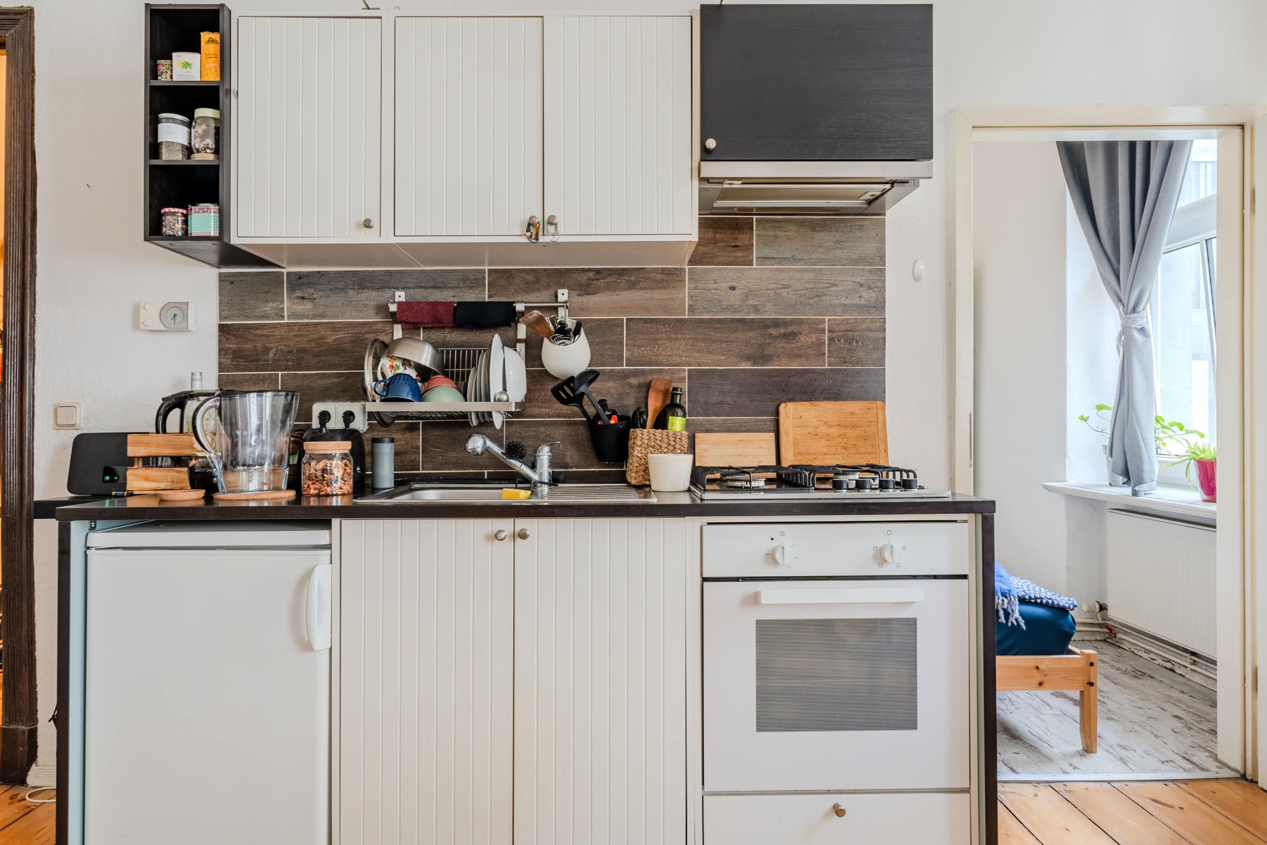 Kompakte Einbauküche in Altbauwohnung von vorne mit Holzfliesenrückwand, weißen Paneelschränken, Gasherd und Kühlschrank