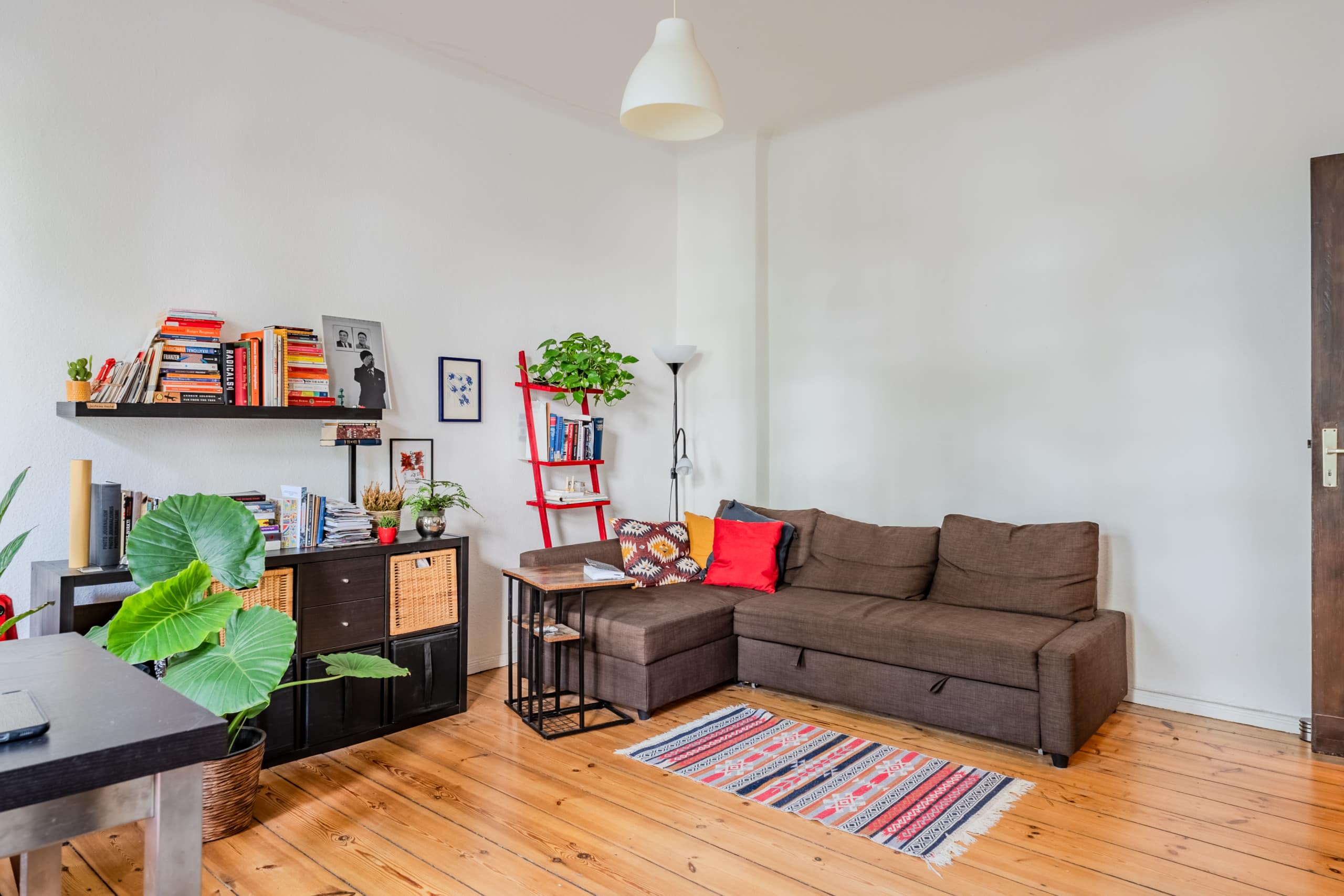 Seitenansicht eines Wohnzimmers in Altbauwohnung mit Parkettboden Ecksofa Bücherregal und Zimmerpflanzen
