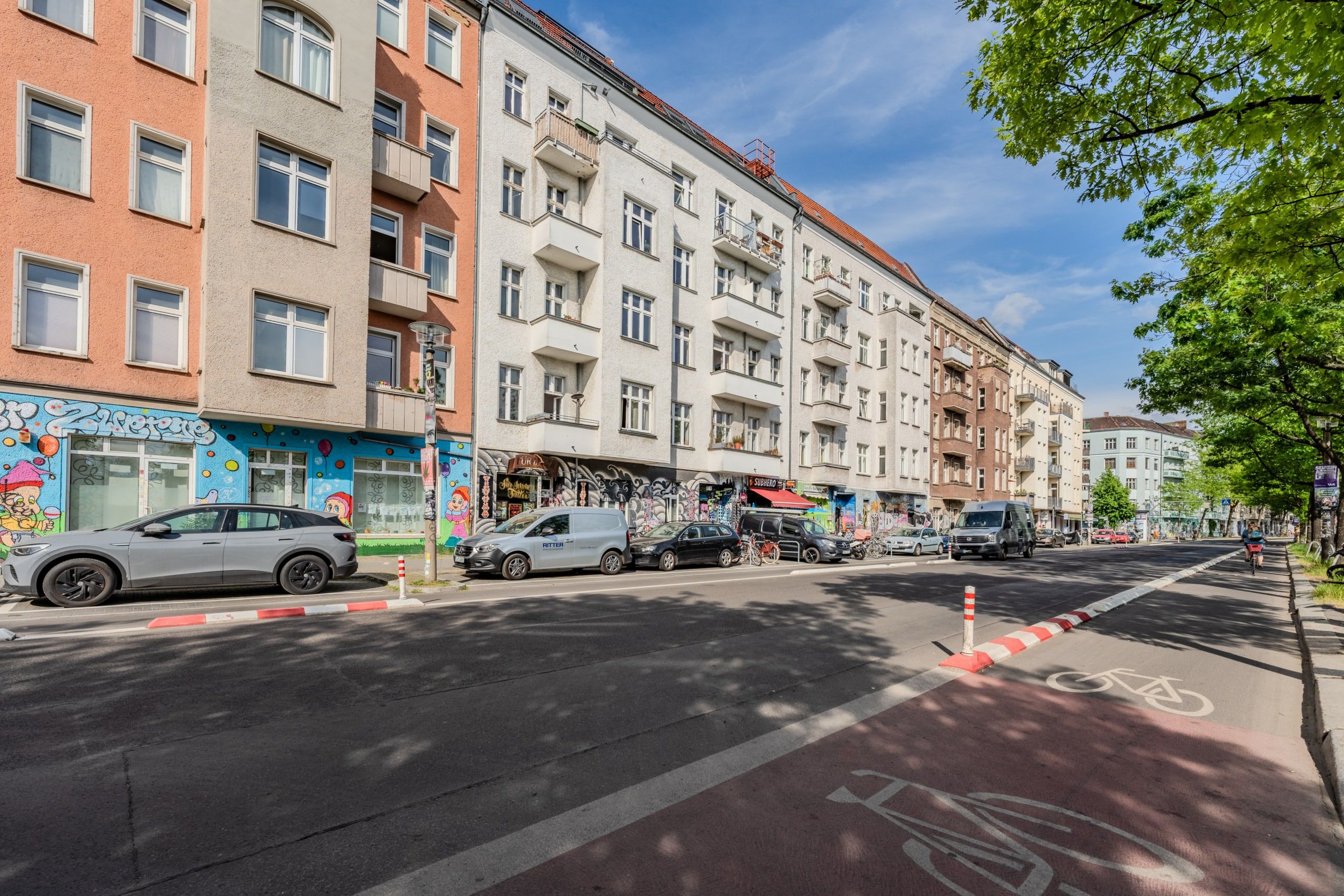 Altbauzeile mit fünf Etagen und Balkonen aus Straßenperspektive helle Putzfassaden Graffiti im Erdgeschoss Fahrradspur