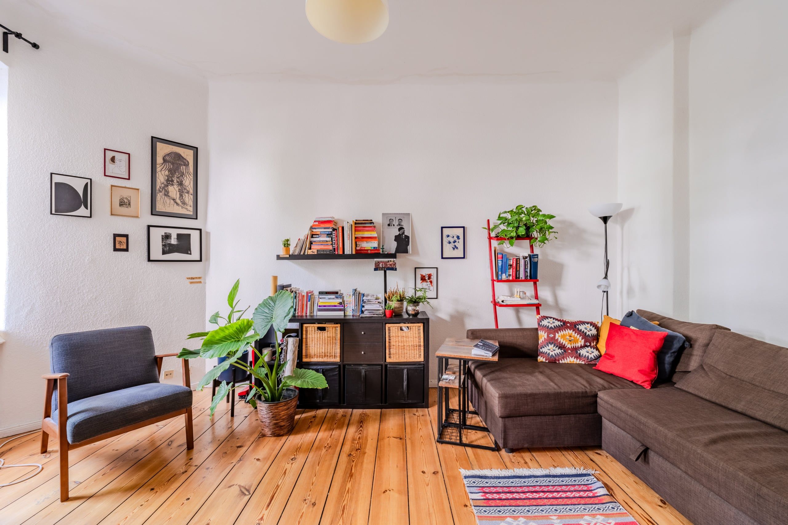 Blick in modern eingerichtetes Wohnzimmer mit Holzdielen, braunem Ecksofa, Bücherregal und Pflanzen