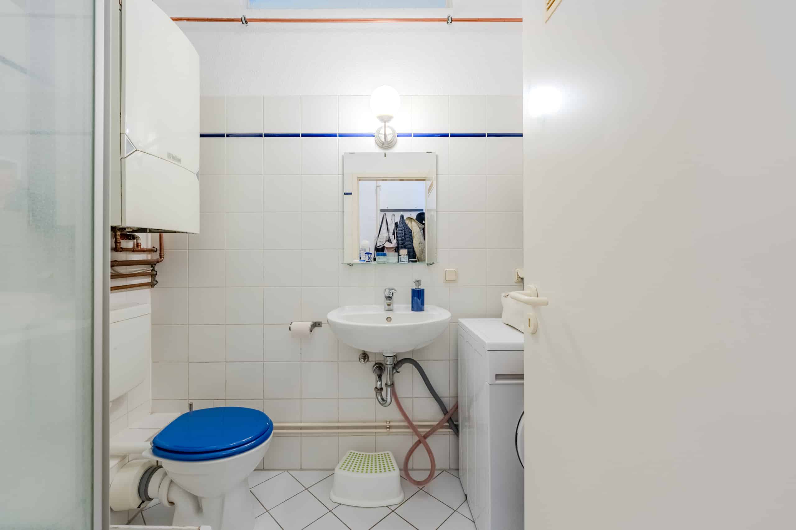 Kleines innenliegendes Badezimmer frontal mit WC mit blauem Sitz, Waschbecken, Spiegel, Ventilationsboiler und Waschmaschine