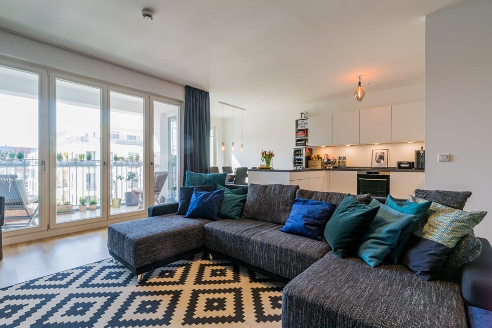 Offener Wohn- und Küchenbereich moderner Stadtwohnung mit bodentiefen Fenstern zu Balkon und großzügiger Eckcouch