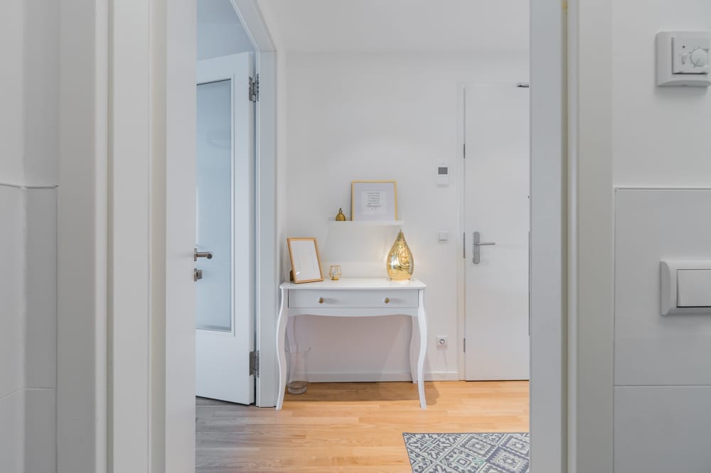 Blick in hellen Wohnungsflur mit weißem Konsolentisch, goldener Lampe und Parkettboden