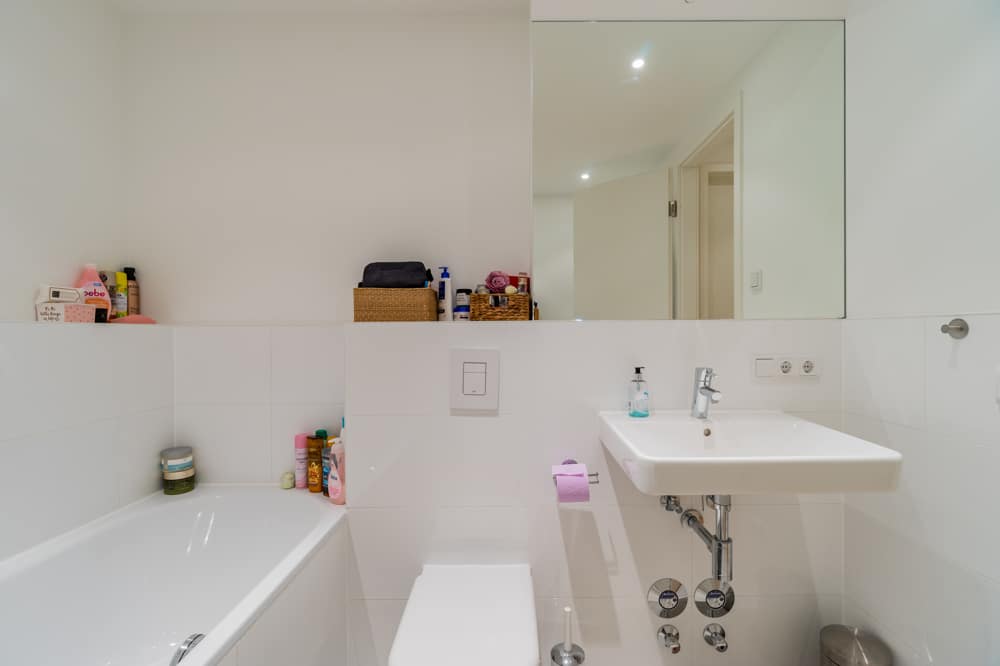 Innenansicht Badezimmer einer Wohnung mit weißer Wandfliese Badewanne wandhängendem WC großem Spiegel und Waschbecken