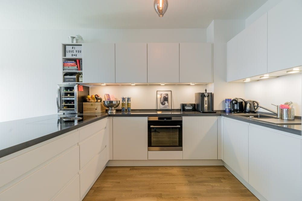 Blick in moderne weiße U-förmige Einbauküche mit schwarzer Arbeitsplatte, eingebautem Herd und Ober- und Unterschränken
