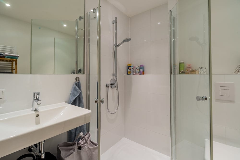 Innenansicht Badezimmer mit ebenerdiger Dusche mit Glasabtrennung Handtuchregal und wandhängendem Waschbecken