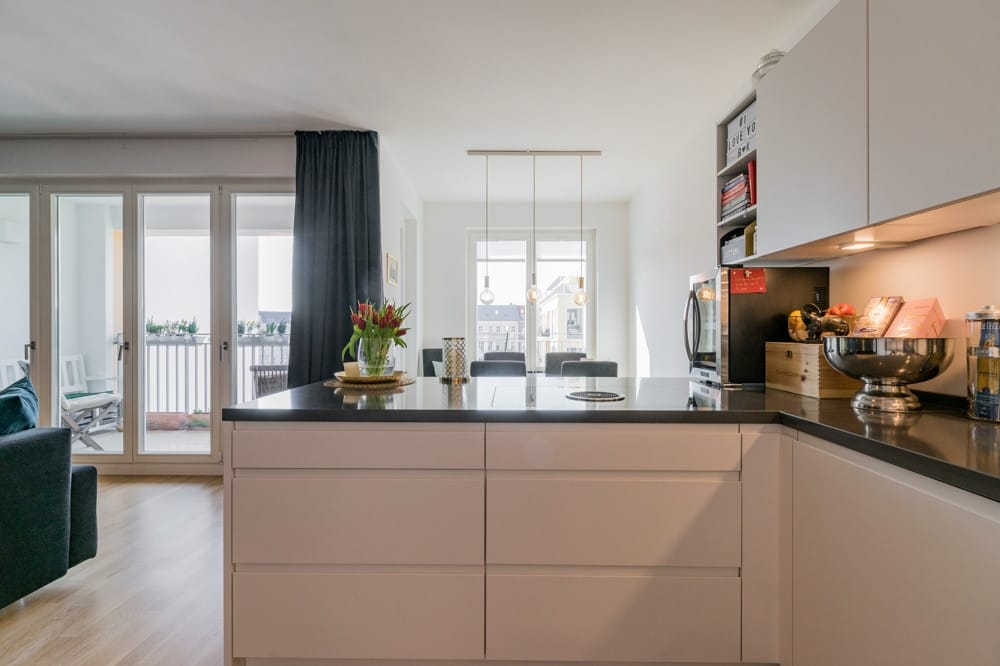 moderne offene Wohnküche mit schwarzer Arbeitsinsel raumhohe Fenster zum Balkon und Esstisch