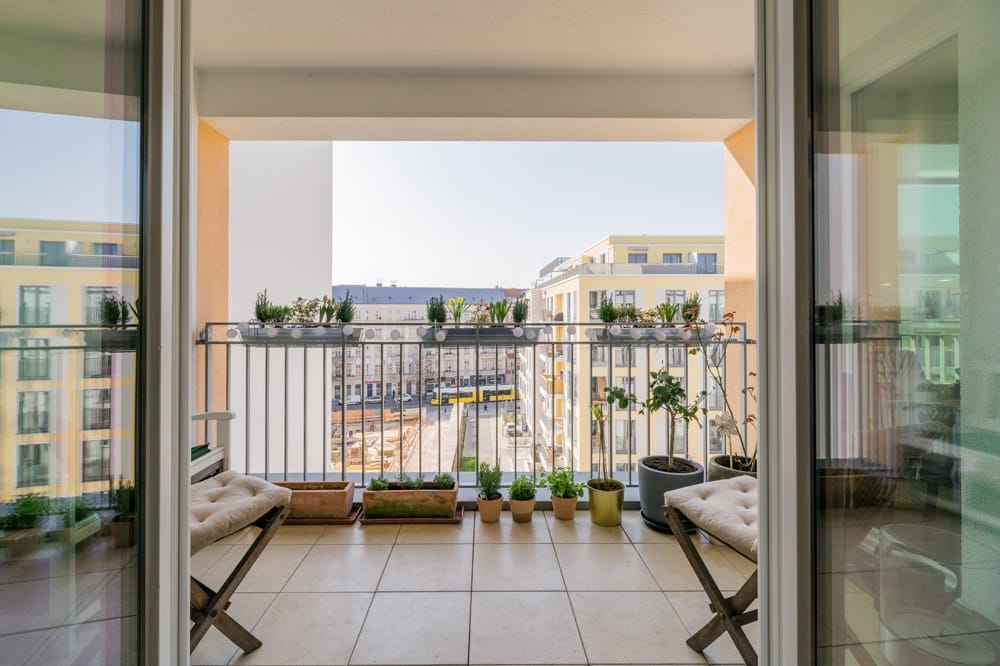 Balkon eines Neubauapartments mit Fliesenboden und Pflanzkästen mit Blick auf gelbe Wohnhäuser im Innenhof
