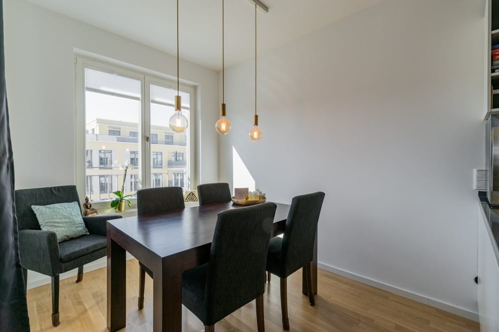 Moderner Essbereich in Neubauwohnung aus Eckperspektive mit dunklem Holztisch und Polsterstühlen