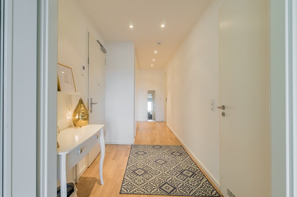 Moderner Eingangsflur mit hellem Holzfußboden Teppichlauf und weißer Pultkommode mit goldener Lampe aus zentraler Perspektive