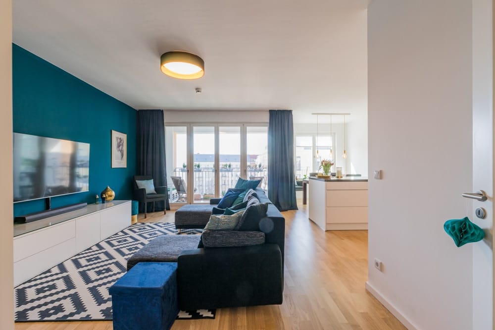 Offener Wohnbereich in moderner Wohnung mit Couch, TV-Wand, Kücheninsel und Balkon mit bodentiefen Fenstern