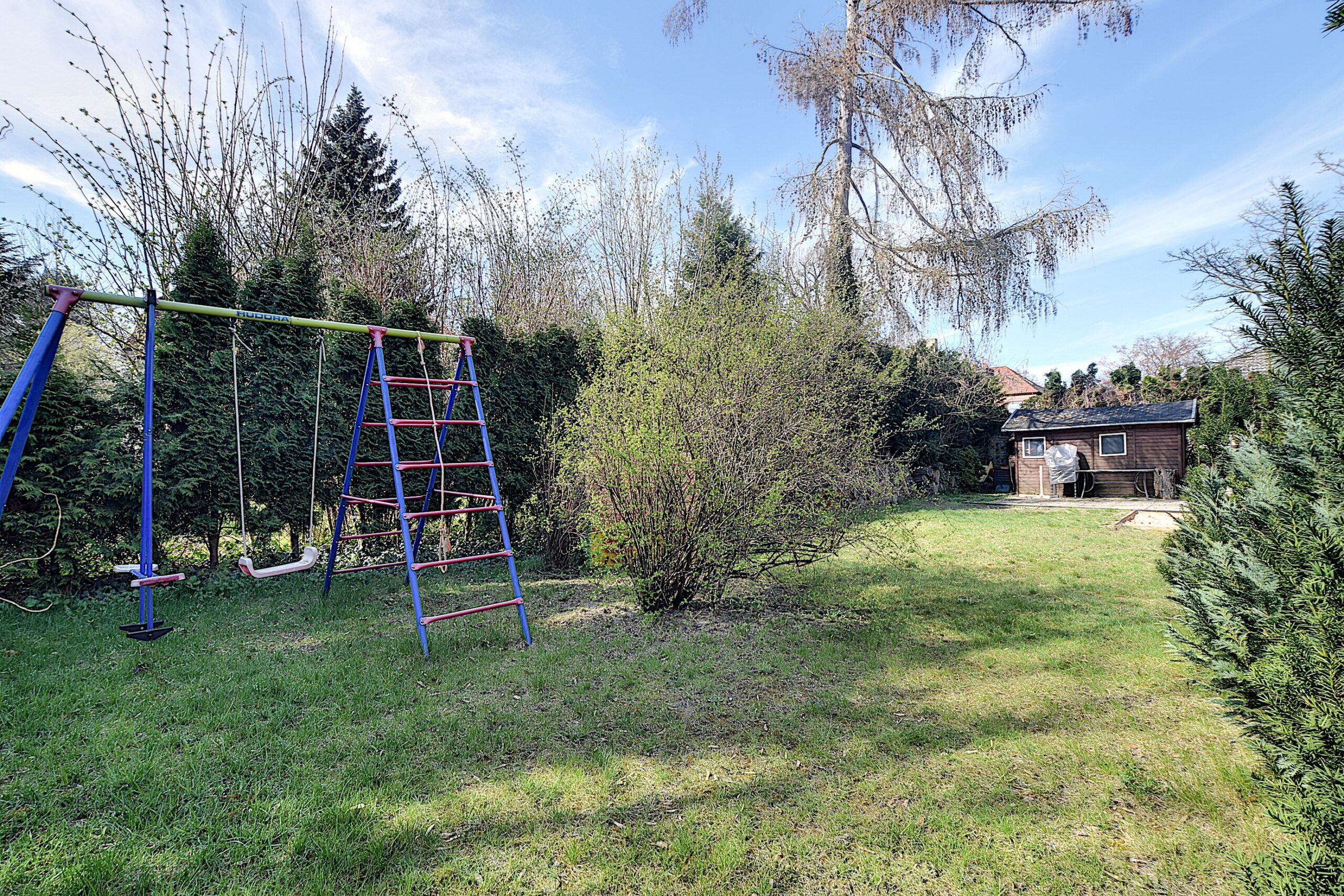 Uitzicht op de tuin met gazon, klimrek en tuinhuisje op de achtergrond