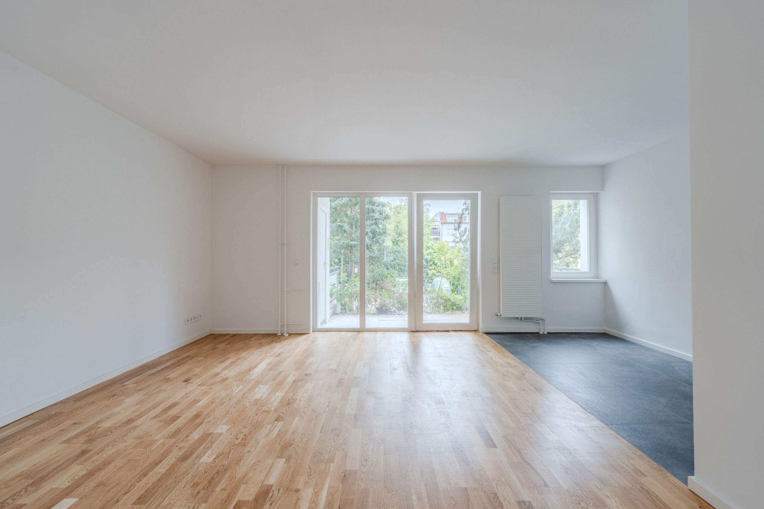 Frontalansicht eines leeren modernen Wohnbereichs mit Parkettboden bodentiefen Fenstern und Terrasse