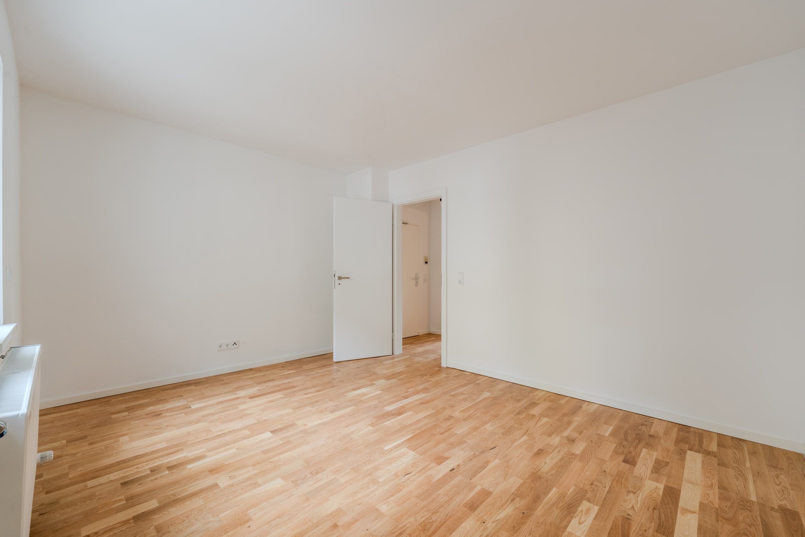 Innenansicht einer Wohnung mit hellem Parkettboden weißen Wänden und offener Tür aus Raumecke fotografiert