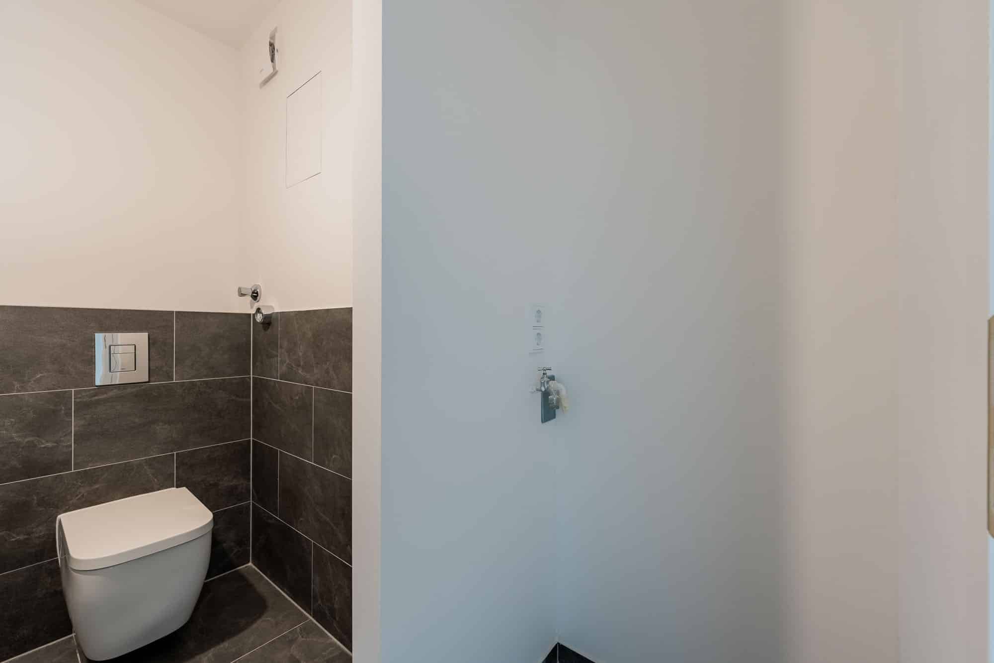 Innenaufnahme Gäste-WC mit wandhängendem WC anthrazitgraue Fliesen halbhoch und seitlichem Wasseranschluss