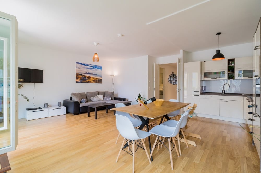 Offenes Wohnzimmer mit Essbereich und moderner weißer Einbauküche auf Parkettboden, Sofa, Esstisch mit Stühlen