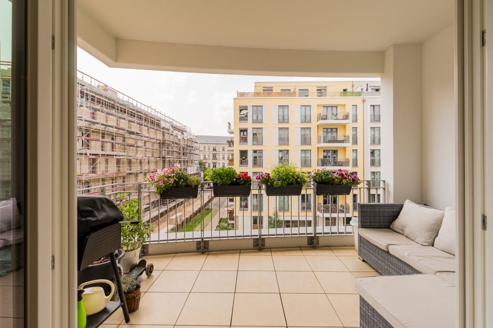Balkon einer Stadtwohnung mit Loungeecke und Blumenampeln vor modernen Mehrfamilienhäusern
