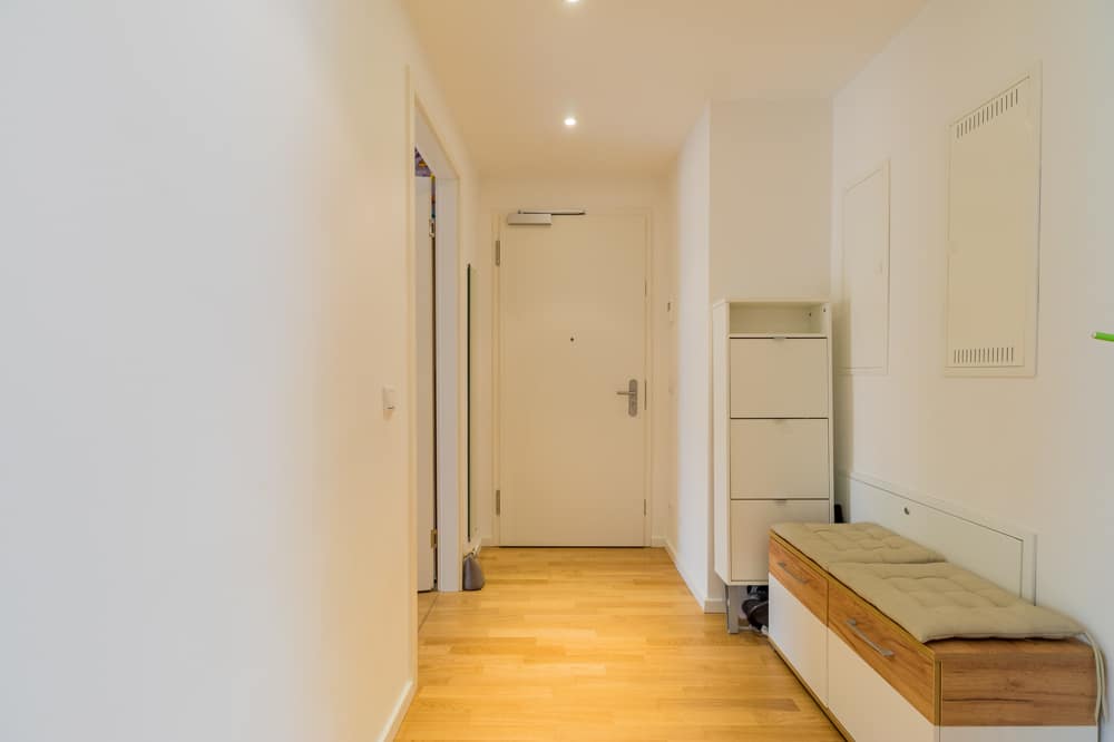 Innenansicht Flur einer Wohnung mit hellen Holzdielen, Eingangstür und weißem Garderobenmöbel