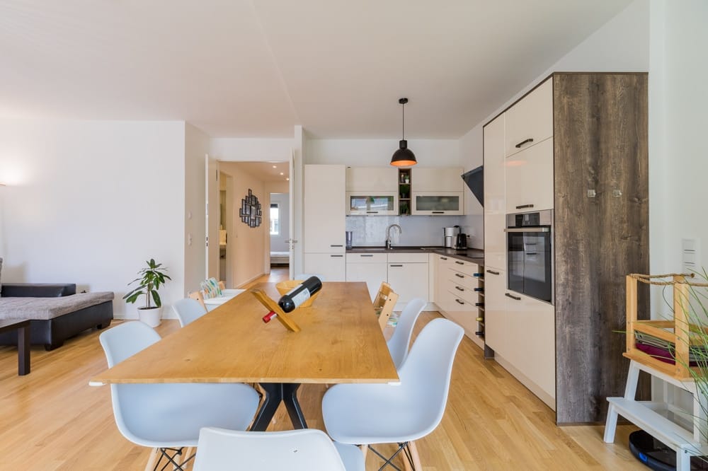 offene Wohnküche einer modernen Wohnung mit Holztisch sechs Stühlen helle Einbauküche und Wohnbereich