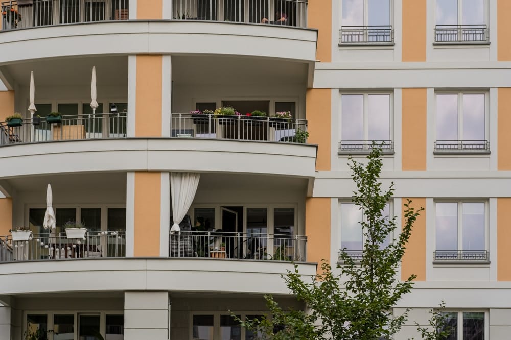 Frontal aufgenommene viergeschossige Wohnhausfassade mit Rundbalkonen und hellgelb-weißer Putzfassade