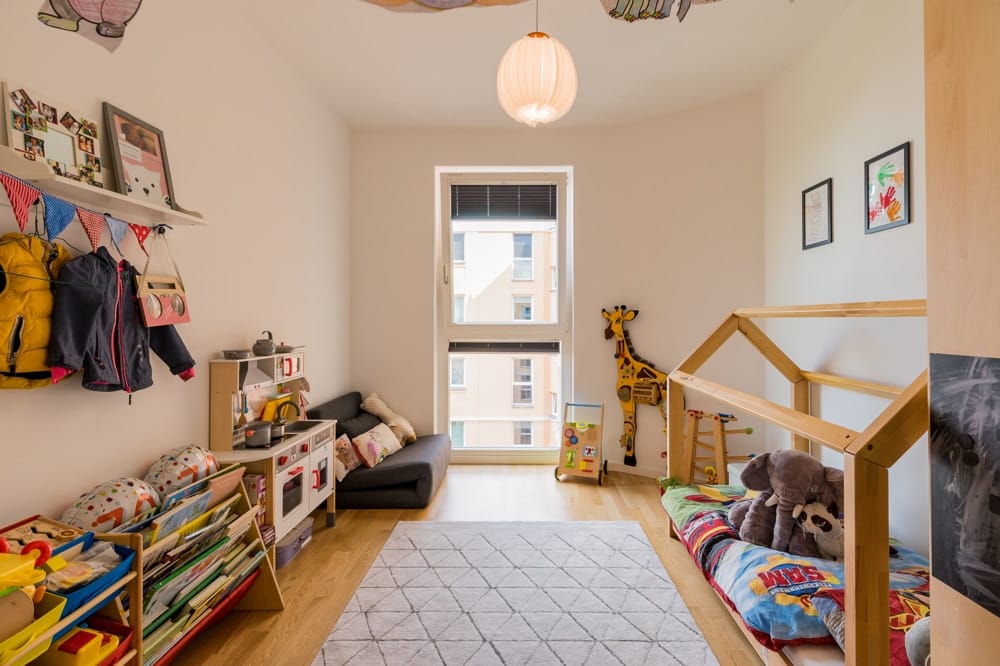Kinderzimmer Innenansicht mit Holzboden offene Fensterfront Spielküche Sofa Regal Spielmatte