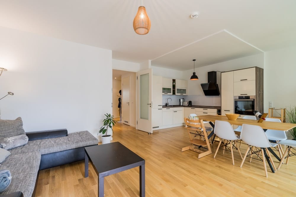 Offener Wohn- und Küchenbereich einer modernen Neubauwohnung mit Holzparkett, Esstisch und Sofa