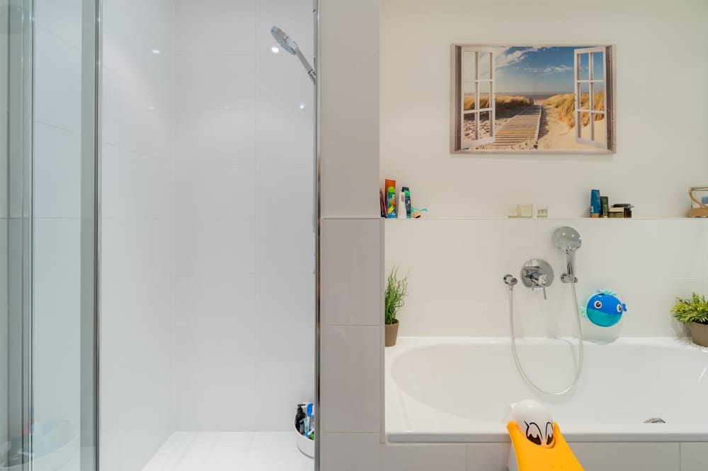 Innenansicht modernes Badezimmer mit Walk-In-Dusche links und Badewanne rechts unter Strandmotiv an weißem Fliesenspiegel