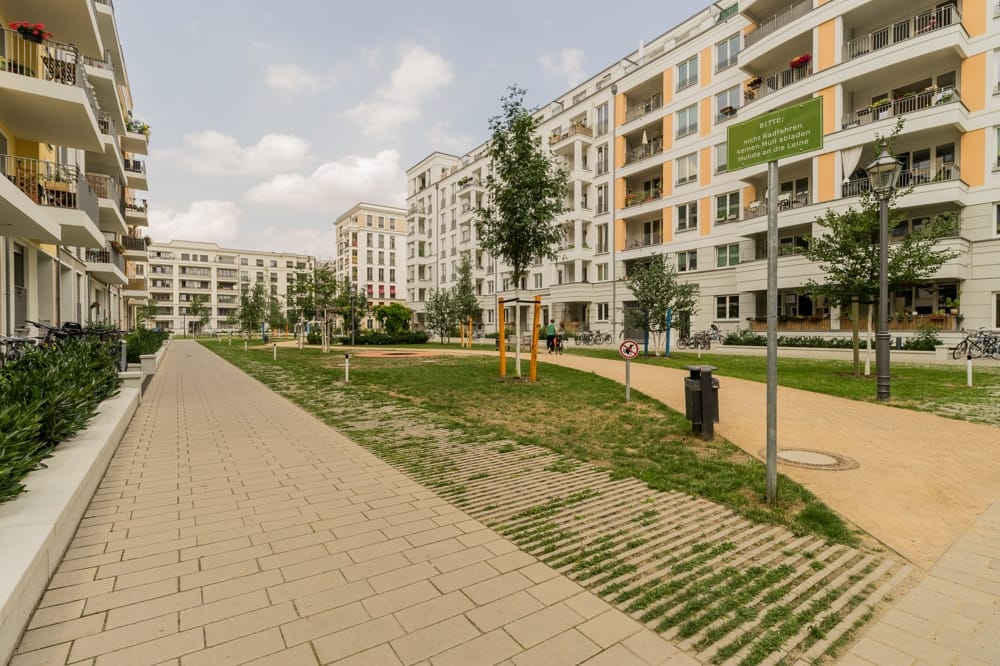seitlicher Blick auf moderne Wohnanlage mit Balkonen begrüntem Innenhof und gepflastertem Weg