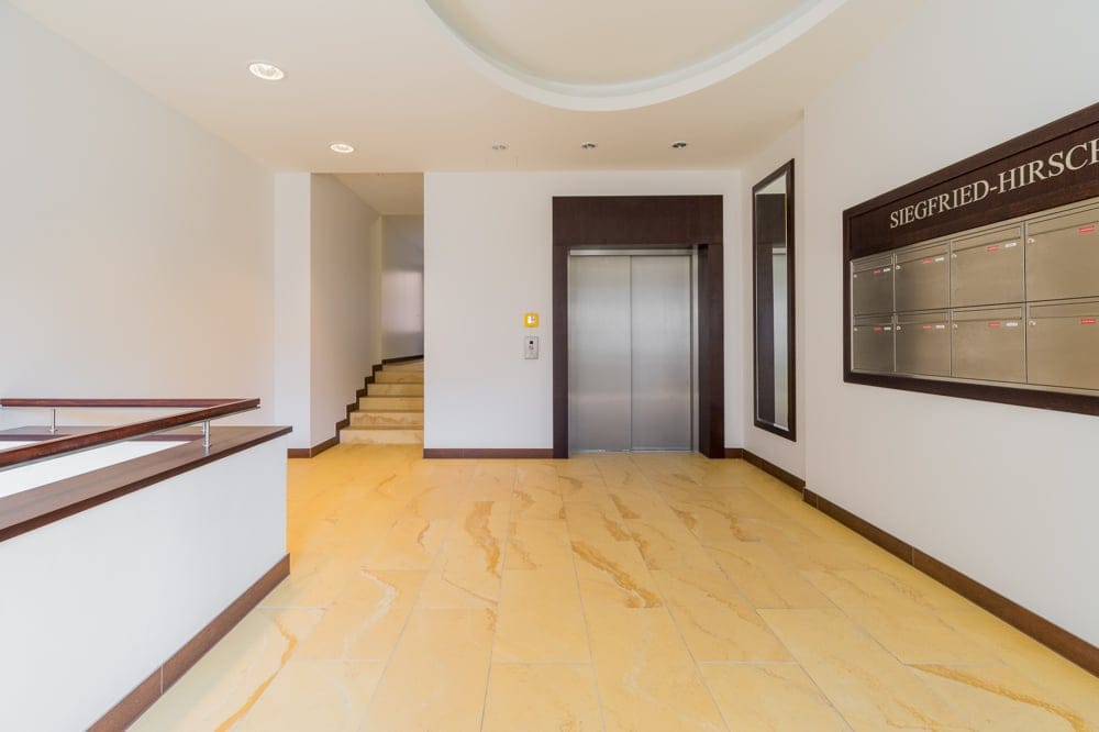 Mehrfamilienhaus-Eingangshalle mit Aufzug, hellbeigem Steinboden, seitlicher Treppe und Wandbriefkästen