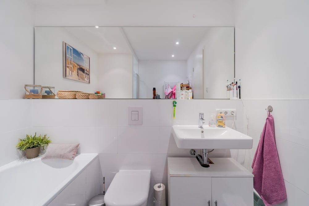 Frontansicht auf modern gefliestes Badezimmer mit Badewanne WC großem Spiegel und weißem Waschtisch