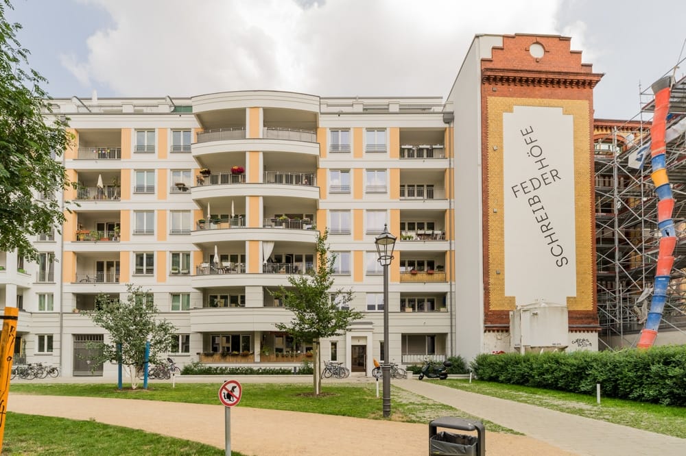 Mehrstöckiges Wohnhaus mit geschwungenen Balkonen und roter Klinkerseitenwand mit Schriftzug Schreibfederhöfe aus Parkblick