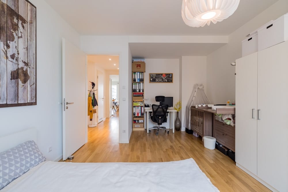 Innenansicht Schlafzimmers mit Arbeitsbereich und Babybett in Neubauwohnung mit Parkettboden und Weltkartenbild an Wand