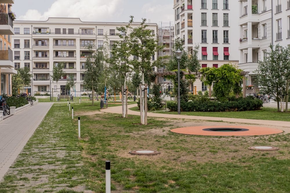 Blick auf modernen mehrgeschossigen Wohnkomplex mit Balkonen und begrüntem Innenhof sowie Spielbereich