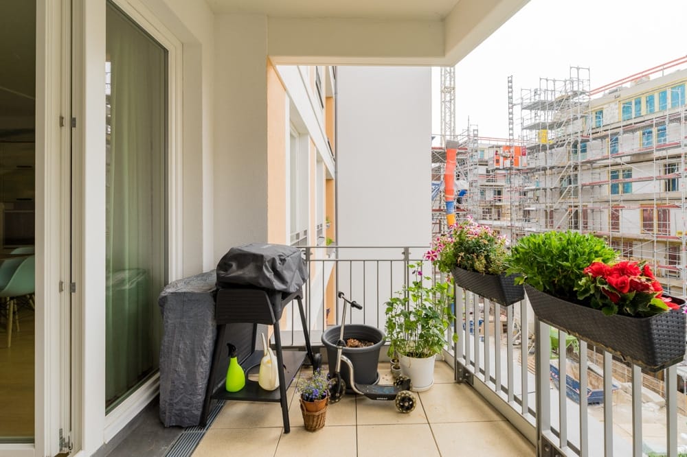 Balkon einer Neubauwohnung von innen mit Blumenkästen, Elektro-Tretroller und Baustelle im Hintergrund