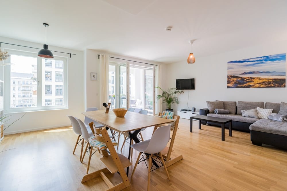 Moderner Wohn-Essbereich mit Holztisch, Stühlen, Sofalandschaft, Parkettboden und Balkon in hellen Räumen