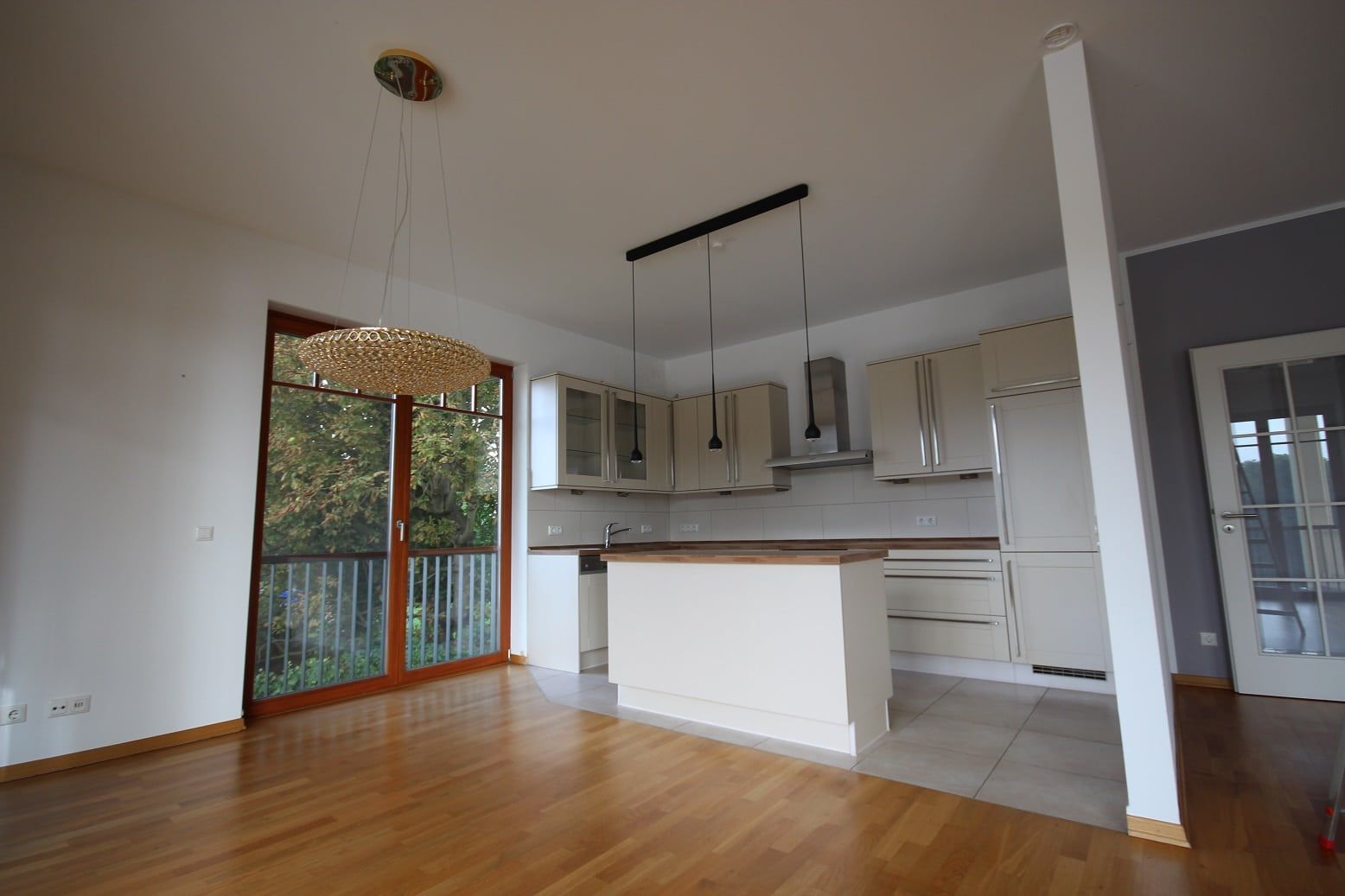Foto degli interni di una zona giorno a pianta aperta con cucina a incasso, isola cucina e accesso al balcone
