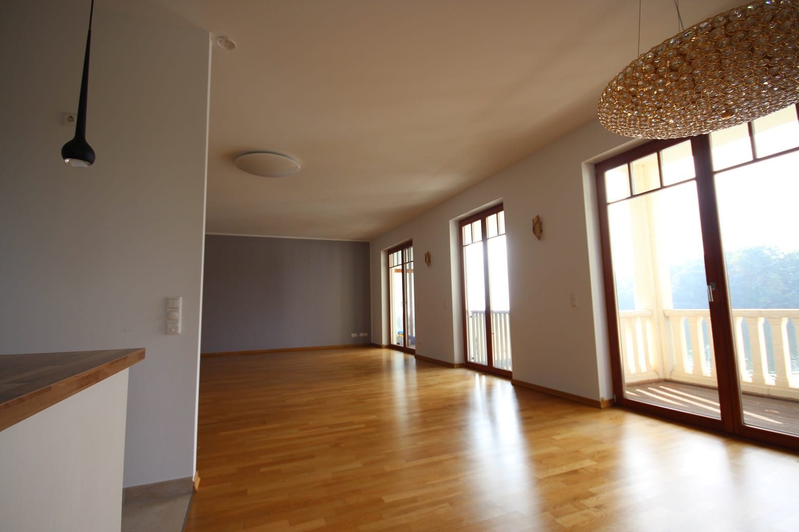 Interno di un soggiorno moderno con pavimento in parquet chiaro, portefinestre a tutta altezza e balcone coperto