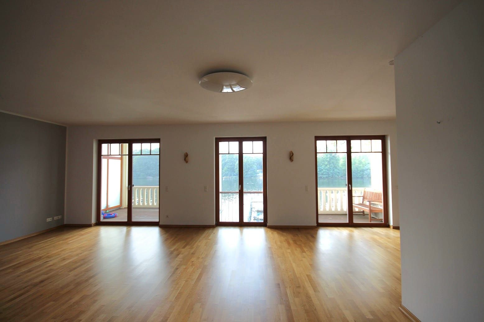 Ampio soggiorno con pavimento in parquet e tre portefinestre a tutta altezza che si affacciano sul balcone con vista sul lago