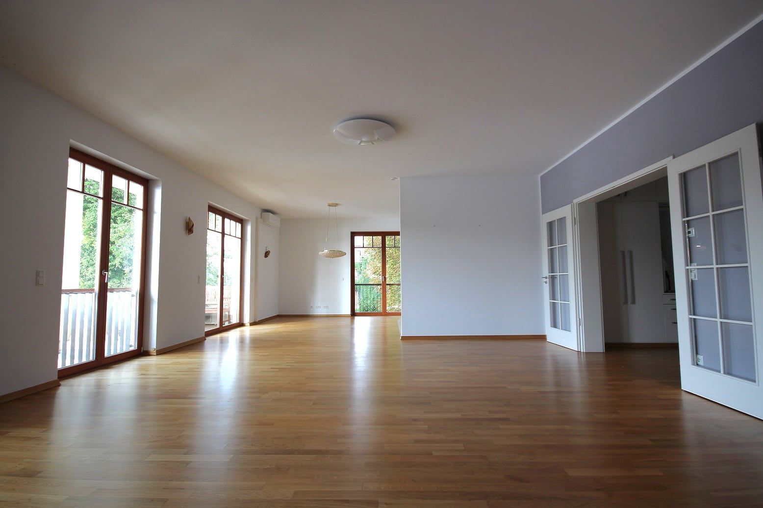 Soggiorno aperto, con ingresso frontale obliquo, pavimento in parquet, finestre a tutta altezza con accesso al balcone e porta a vetri a due ante